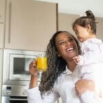 Joyful mother and child bonding in kitchen, holding glass of orange juice, expressing happiness.