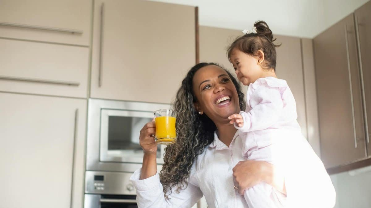 Joyful mother and child bonding in kitchen, holding glass of orange juice, expressing happiness.