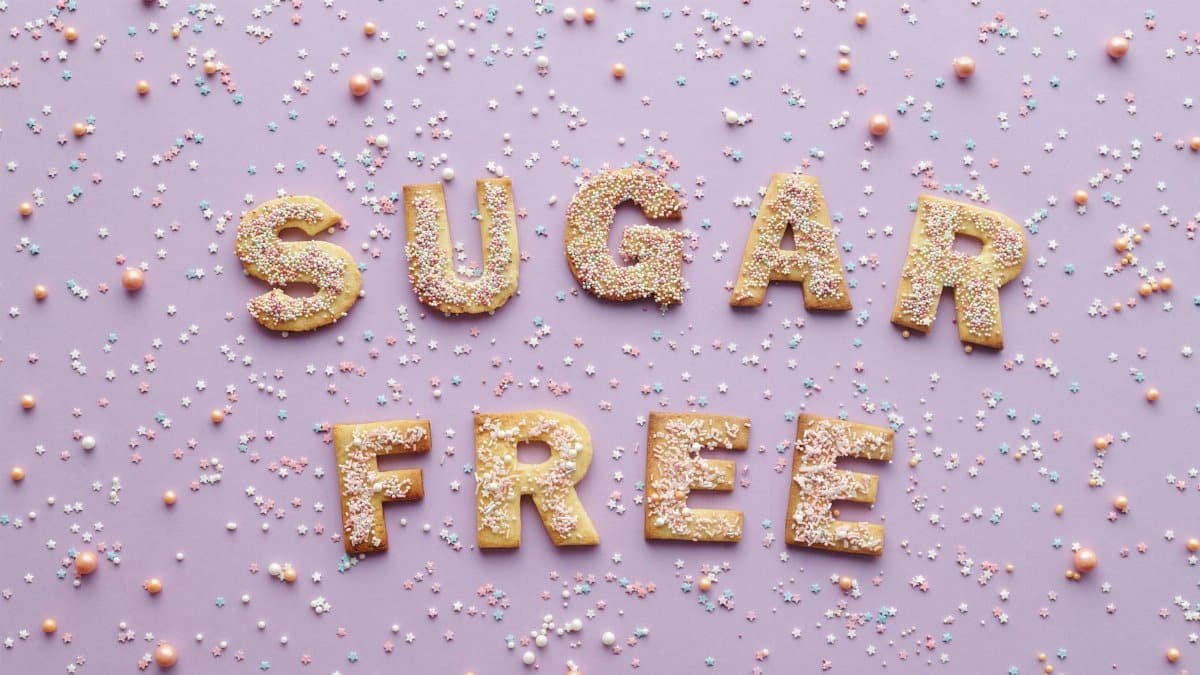 Flatlay of sugar-free cookie letters with sprinkles on a pink background.