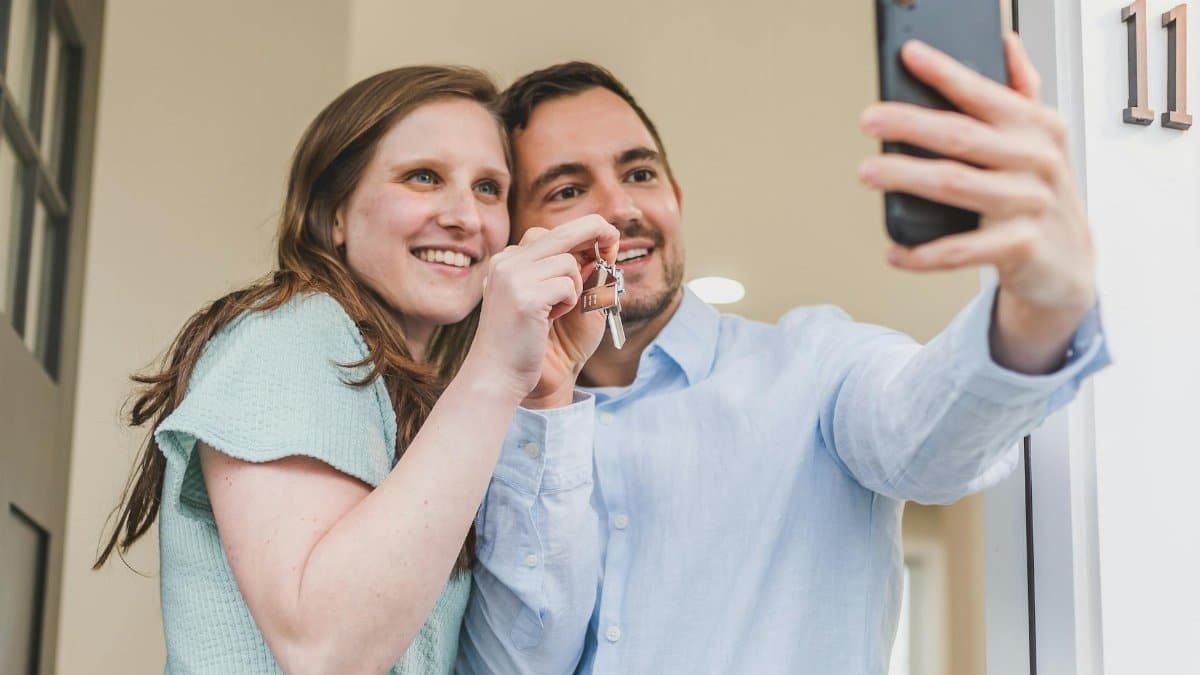 Joyful couple taking a selfie while holding keys to their new home, celebrating a milestone.