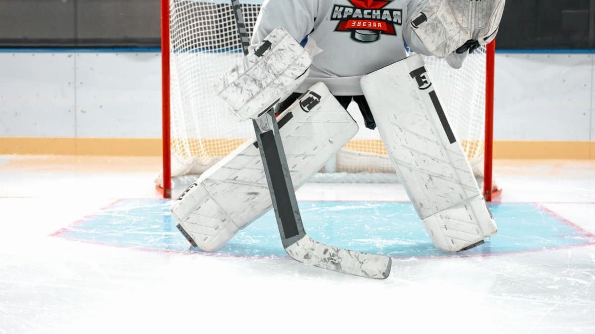 Ice hockey goalie in full gear guarding the net during an intense game on the ice rink.