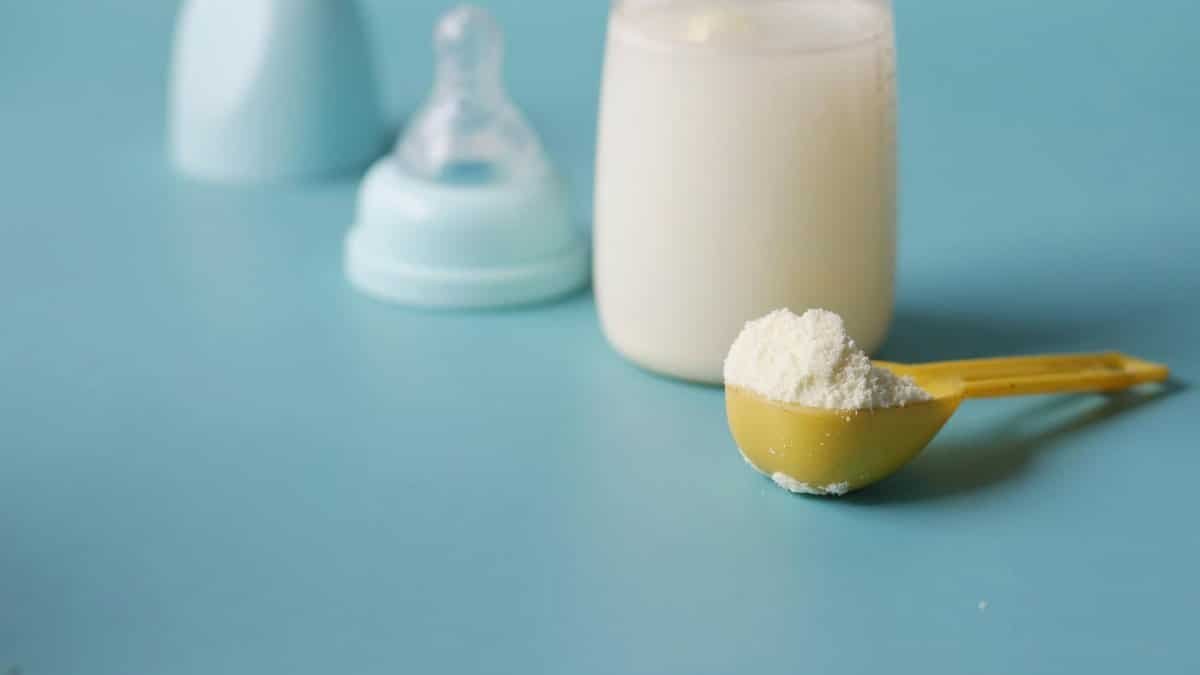 Close-up of baby milk formula powder in a yellow scoop with a bottle on a blue background.