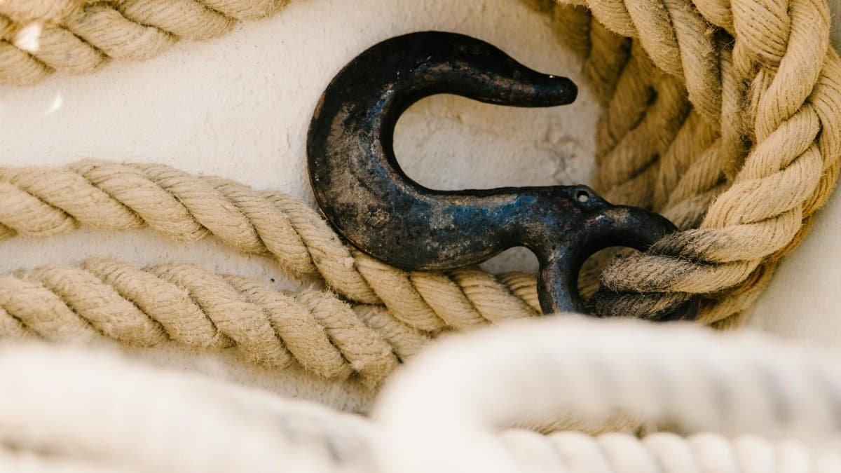 Close-up of a rustic metal hook entwined with thick ropes on a white surface, emphasizing texture.