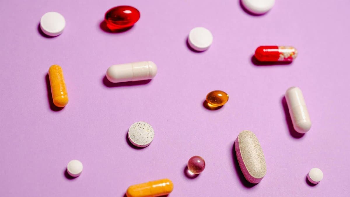 Various colorful pills and capsules scattered on a purple surface, representing healthcare and medication.