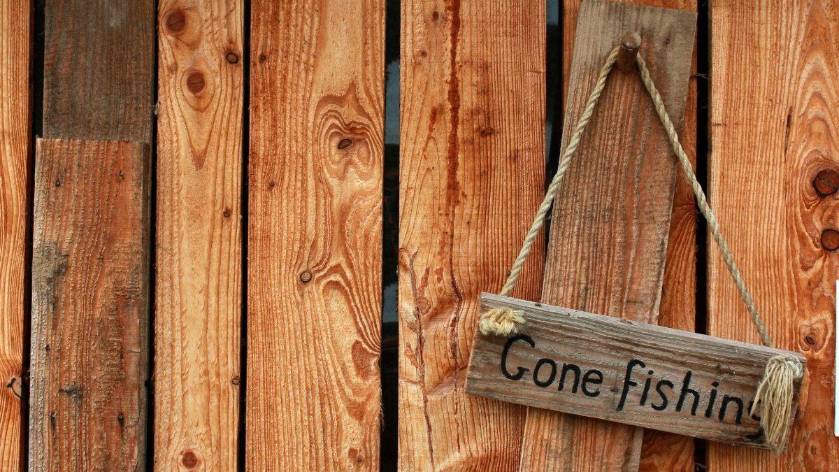 Wooden fence with a rustic 'Gone Fishing' sign hanging, perfect for outdoor and rustic decor themes.