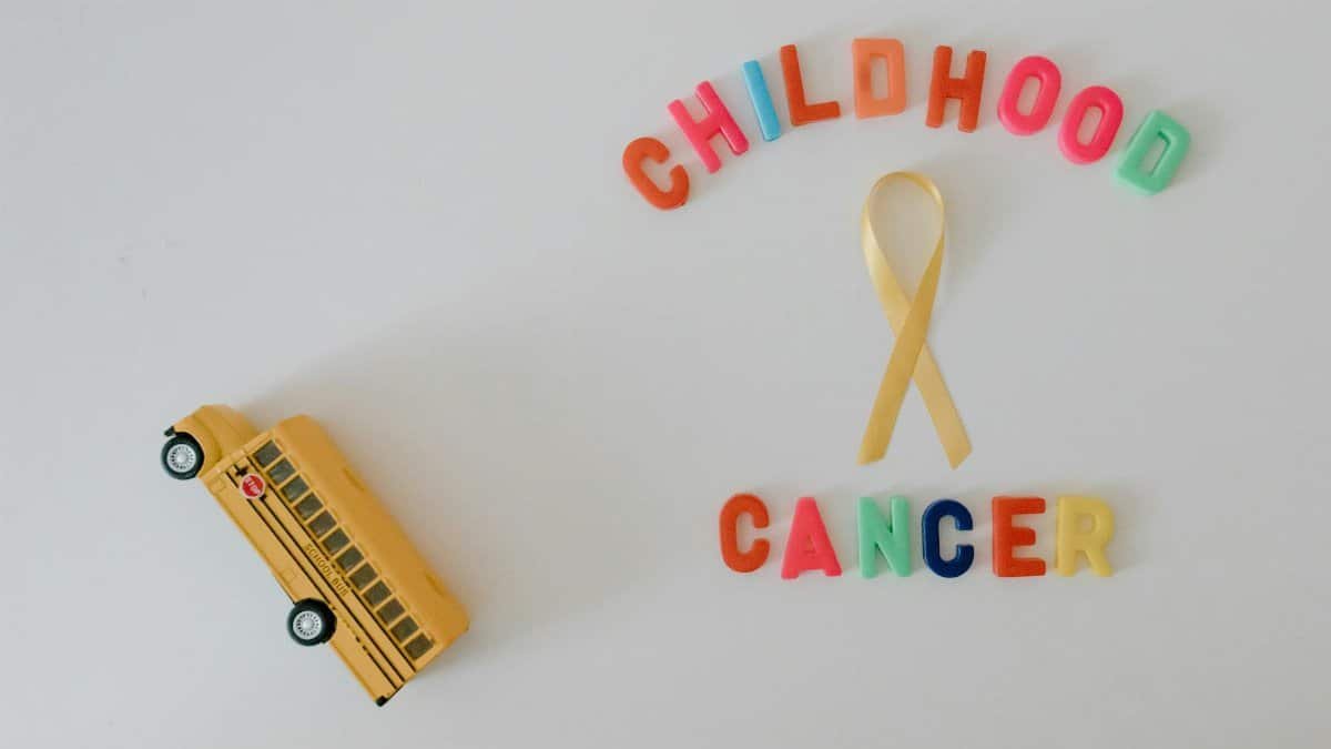 Colorful display of childhood cancer awareness with toy school bus and ribbon on white background.