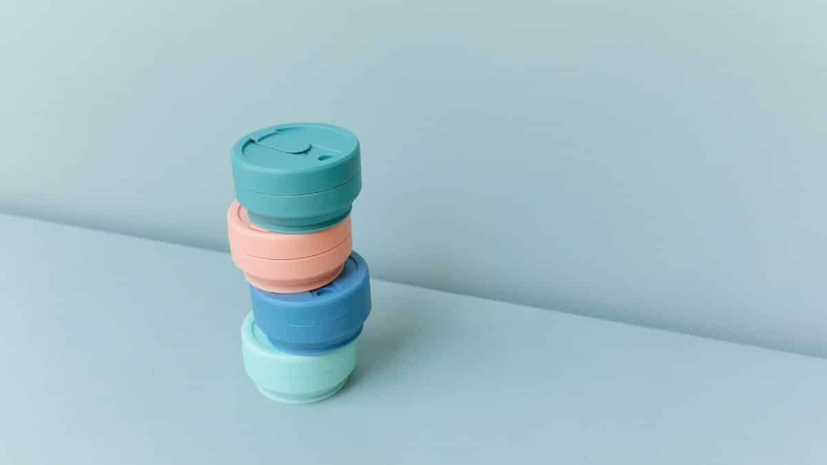 Minimalist image of stacked reusable cup lids in pastel colors on a plain blue surface.