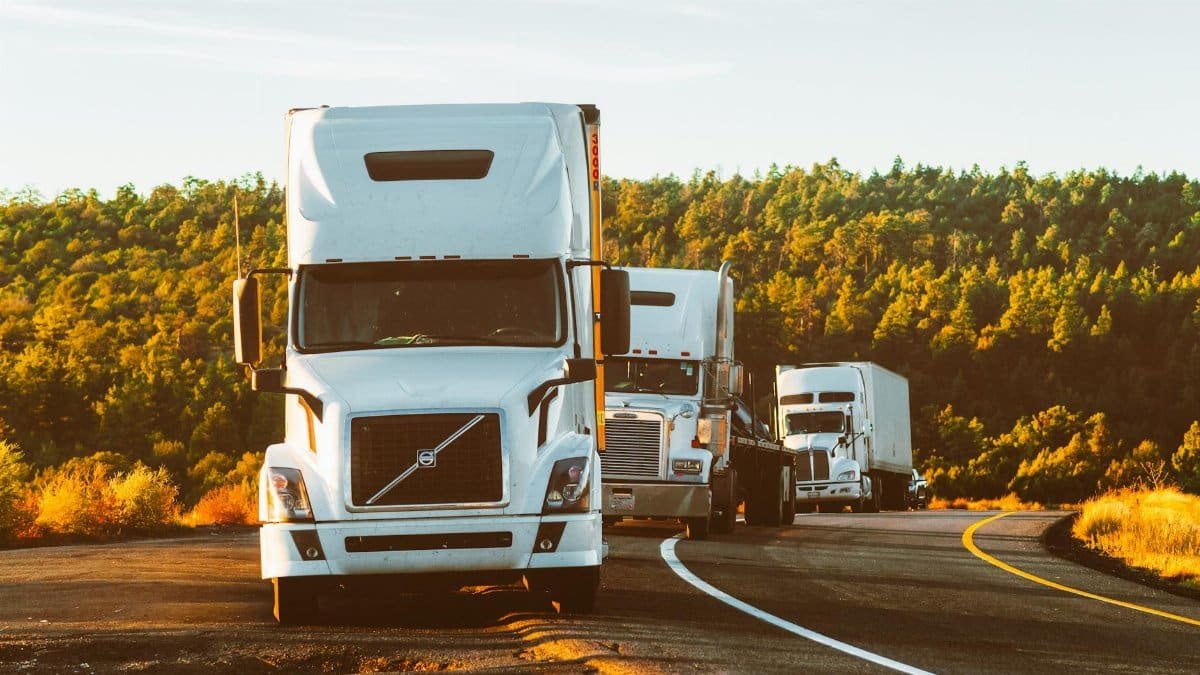 Three semi trucks driving on a highway through a forested landscape in Arizona.