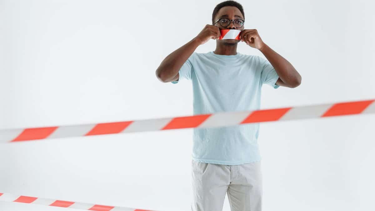 Adult man posing with barricade tape on mouth, studio shot. Conceptual image of silence and protest.