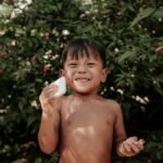 A smiling child holding a bar of soap outdoors among lush greenery, evoking a sense of cleanliness and happiness.