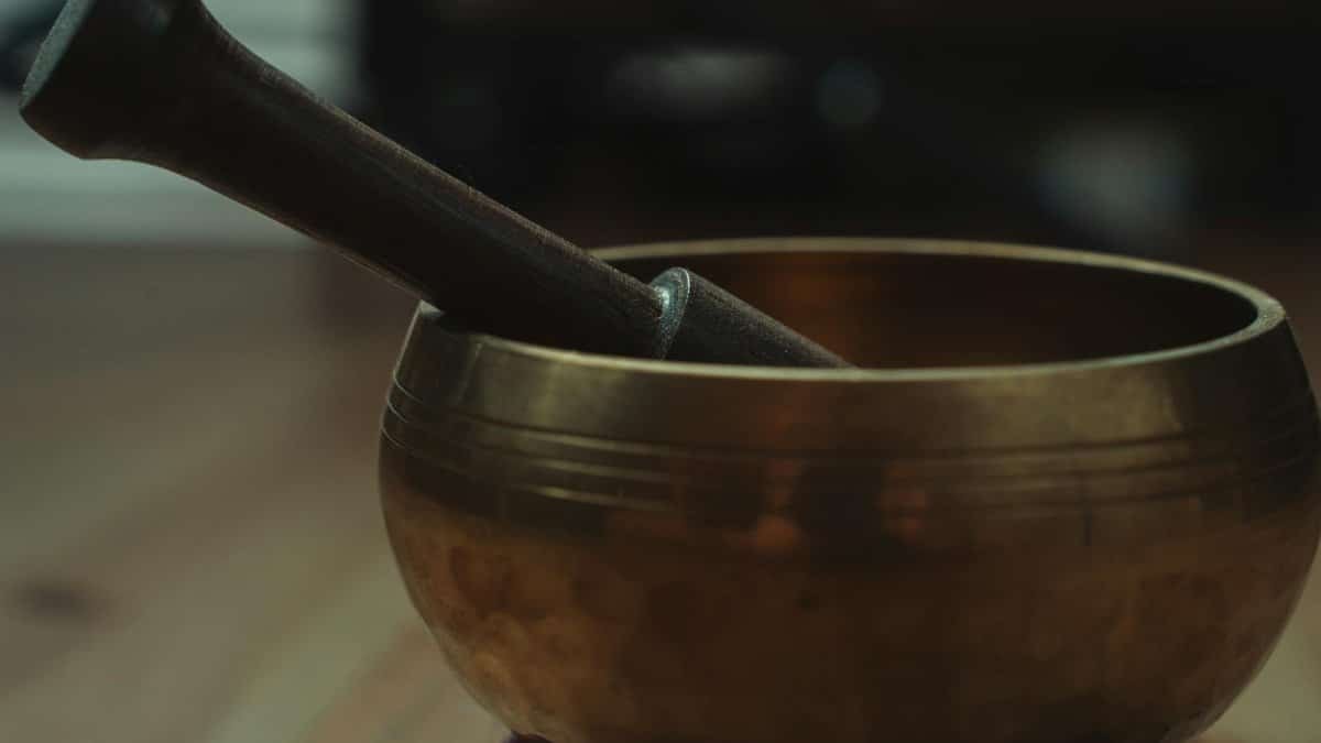 A detailed view of a bronze Tibetan singing bowl and wooden mallet used in meditation and sound therapy.