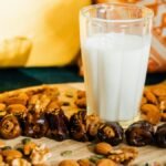A refreshing glass of milk surrounded by dates, almonds, and nuts on a wooden board.