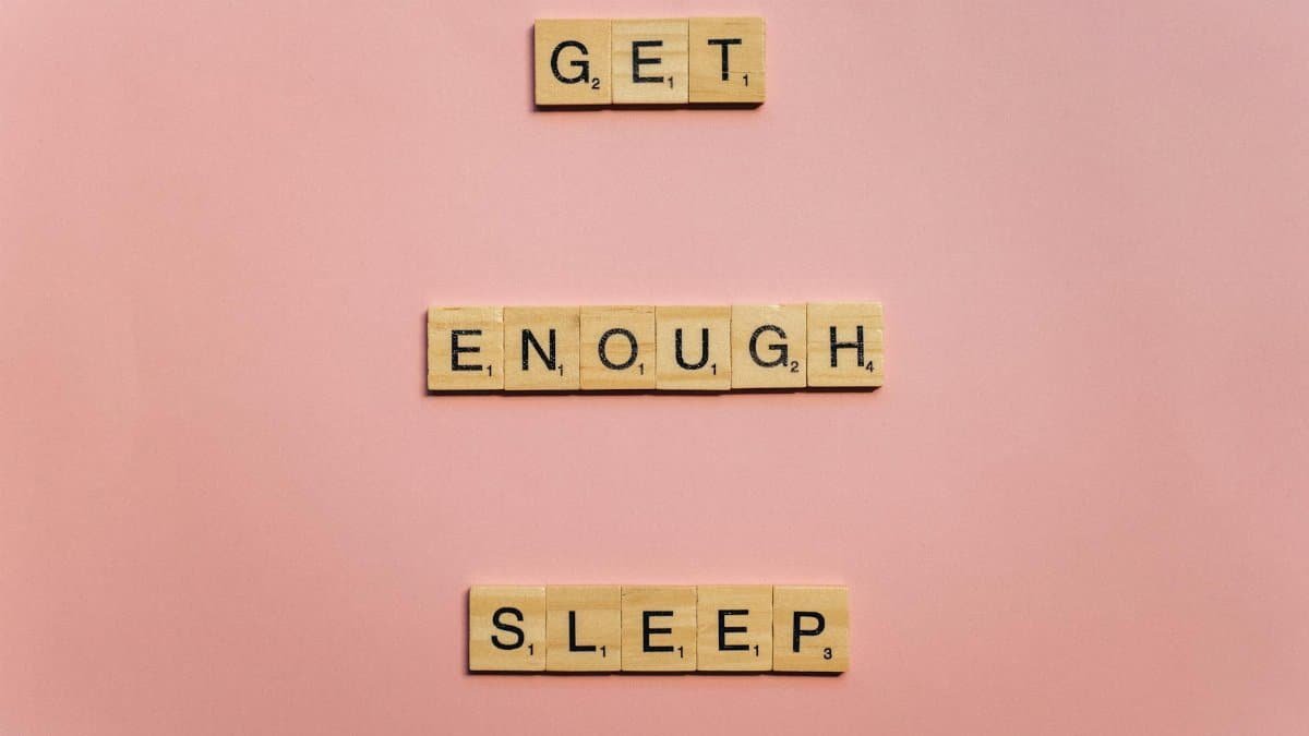 Scrabble tiles on a pink background spelling out 'Get Enough Sleep'. Ideal for wellness and lifestyle themes.
