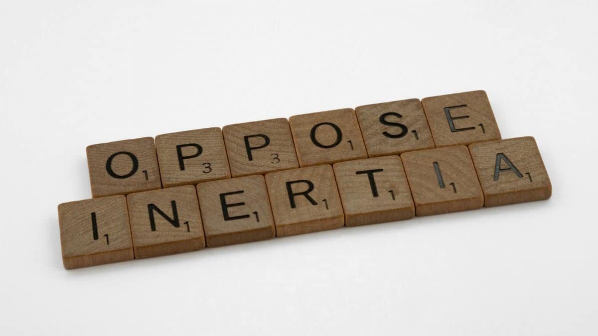 Scrabble tiles spell 'oppose inertia' on a white surface, creating inspiration.