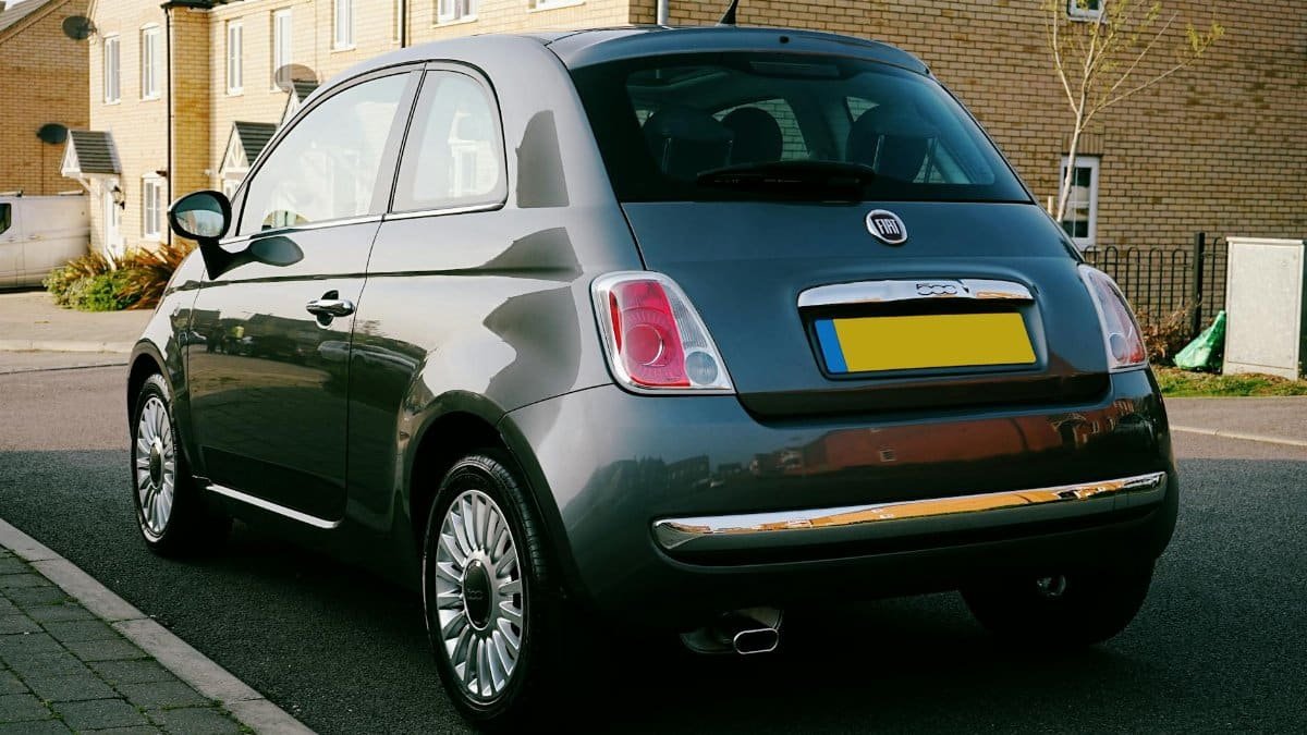 A classic Fiat 500 parked on a suburban street in the UK, featuring a clear sunny day and modern housing.