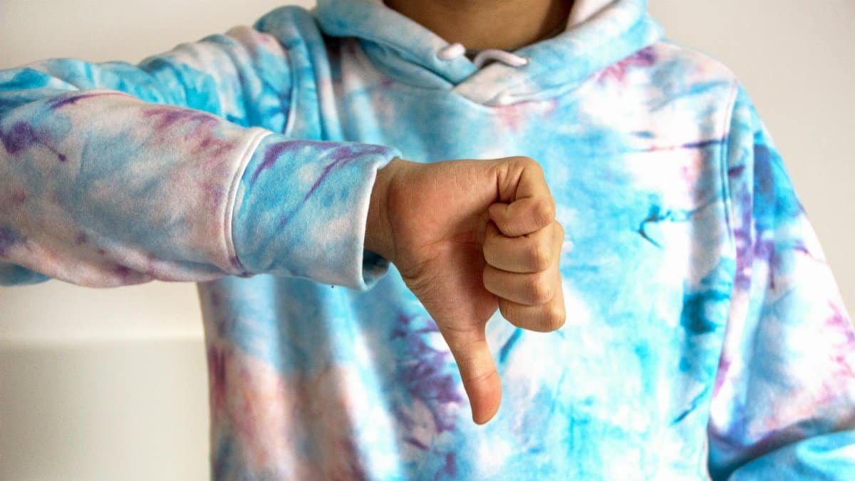 A person wearing a colorful tie-dye hoodie showing a thumbs down gesture, symbolizing disapproval.