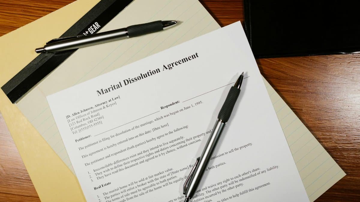 Flat lay of a marital dissolution agreement form with pens and files on a desk.
