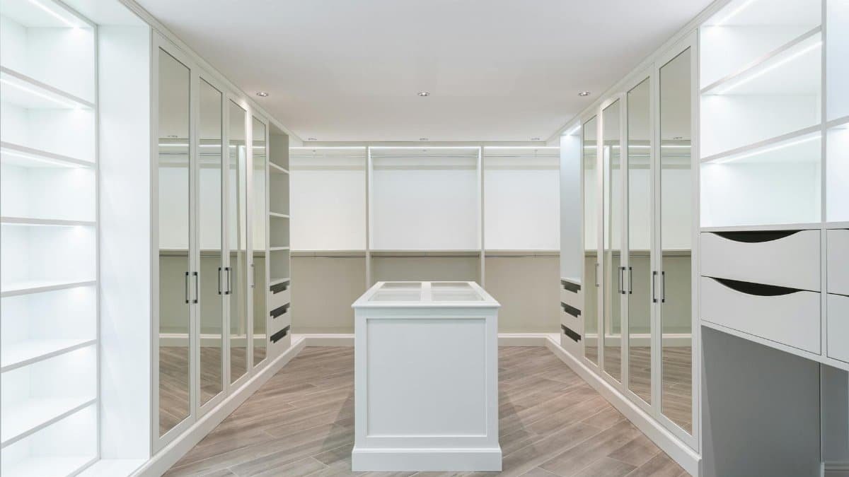 A contemporary and spacious walk-in closet with mirrored doors and ample storage space for a luxurious home.
