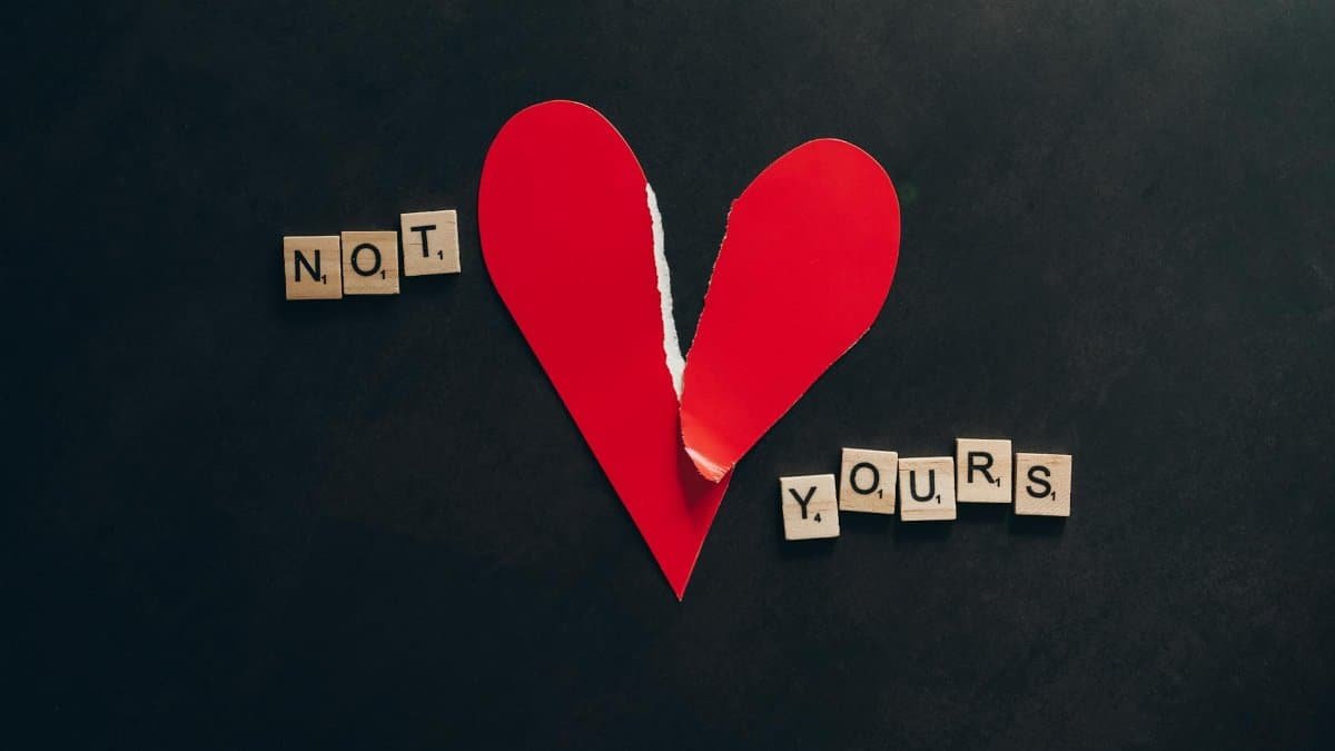 Artistic image of a torn red heart with scrabble tiles spelling 'Not Yours' on a black background.