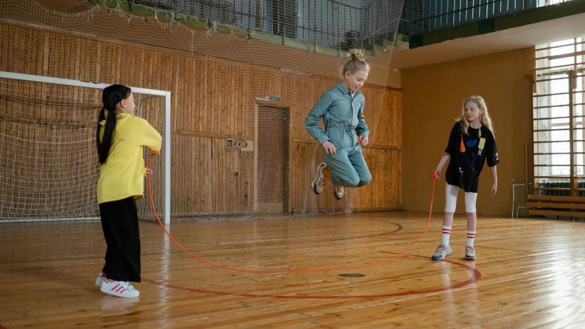 Children having fun with a jump rope during a play session in an indoor gym.