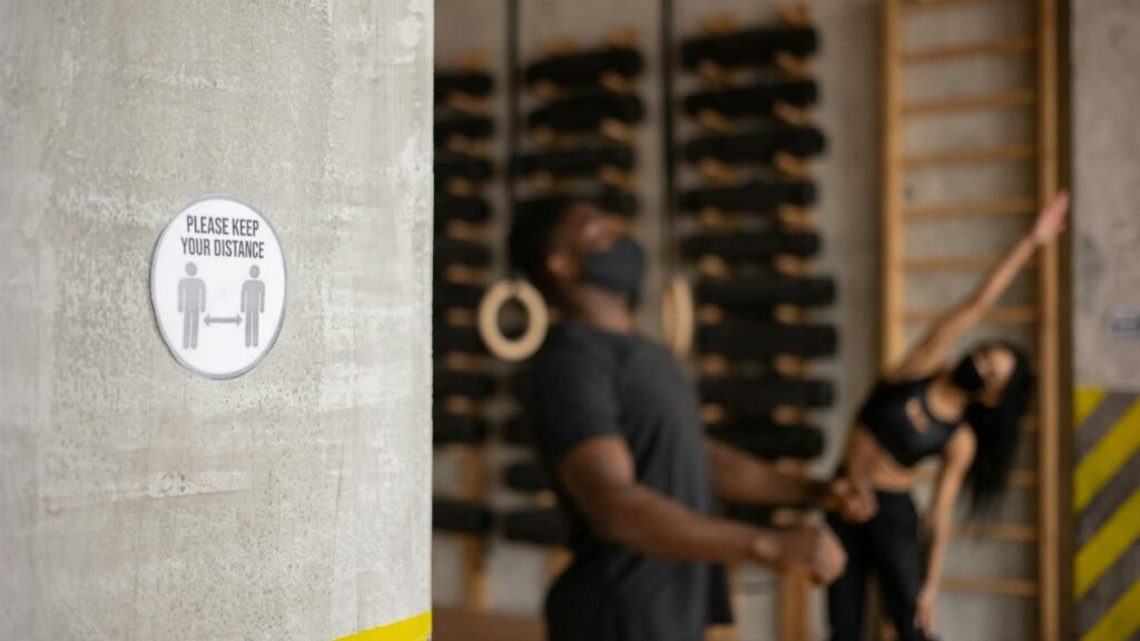 Two people exercising indoors with a social distancing sign prominently displayed.