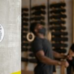 Two people exercising indoors with a social distancing sign prominently displayed.