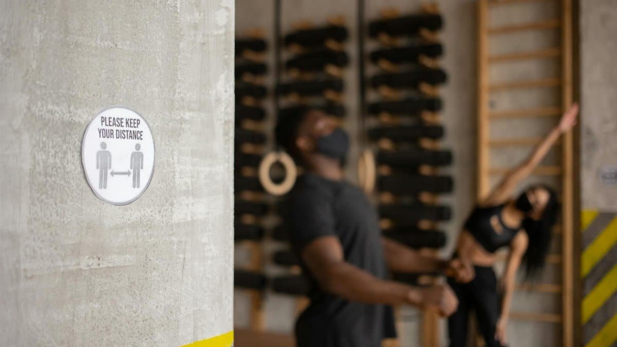 Two people exercising indoors with a social distancing sign prominently displayed.