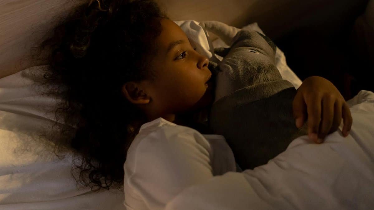 A young girl cuddles a stuffed elephant, looking dreamy and cozy in bed at night.