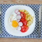 A delicious breakfast featuring fried eggs, tomatoes, radishes, and smashed potatoes.