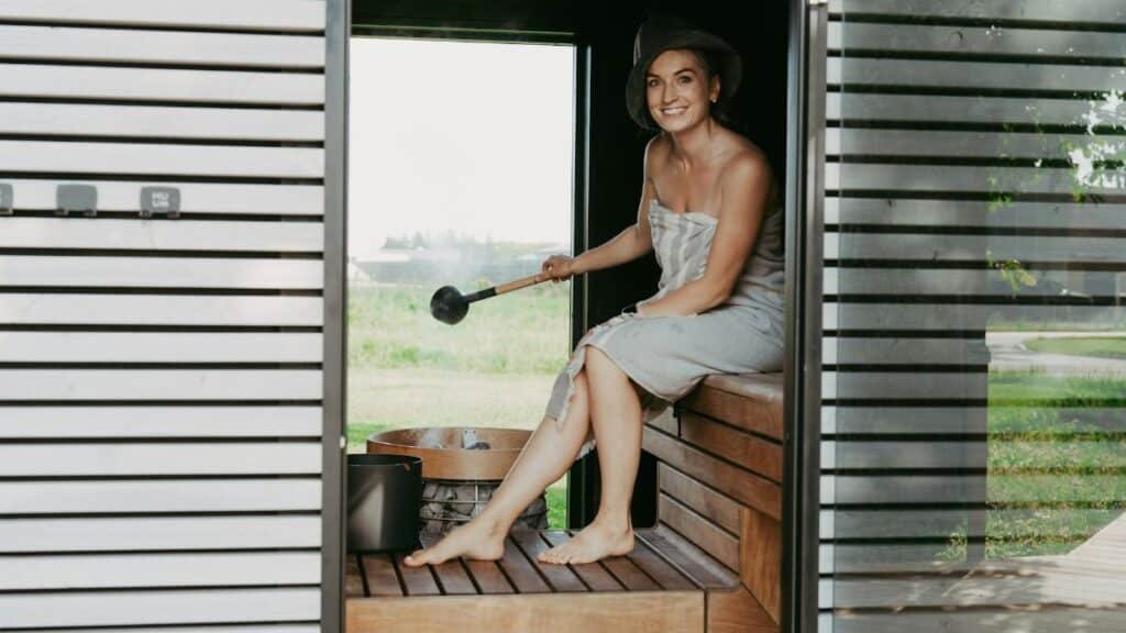 A woman in a sauna, wrapped in a towel, enjoying a relaxing steam session with a sauna hat.