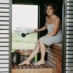 A woman in a sauna, wrapped in a towel, enjoying a relaxing steam session with a sauna hat.