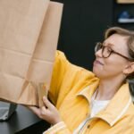 A woman in a store holding a brown paper bag and a credit card, smiling.
