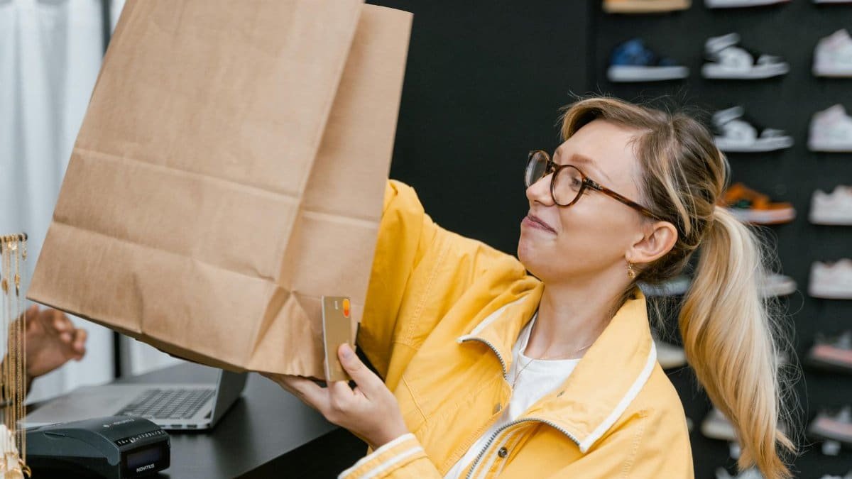 A woman in a store holding a brown paper bag and a credit card, smiling.