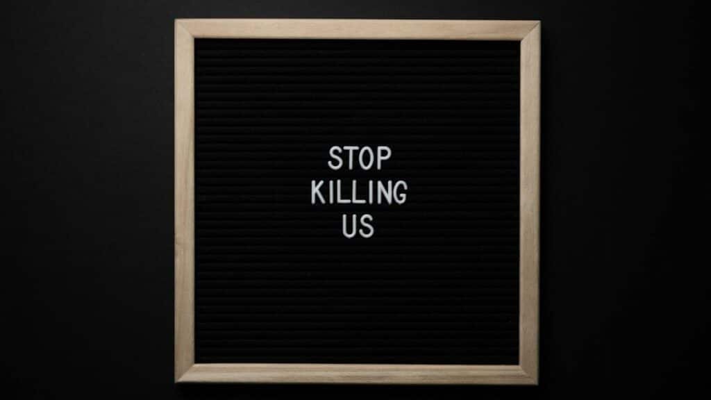 Top view of slogan Stop Killing Us on surface of square blackboard on black background
