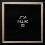 Top view of slogan Stop Killing Us on surface of square blackboard on black background