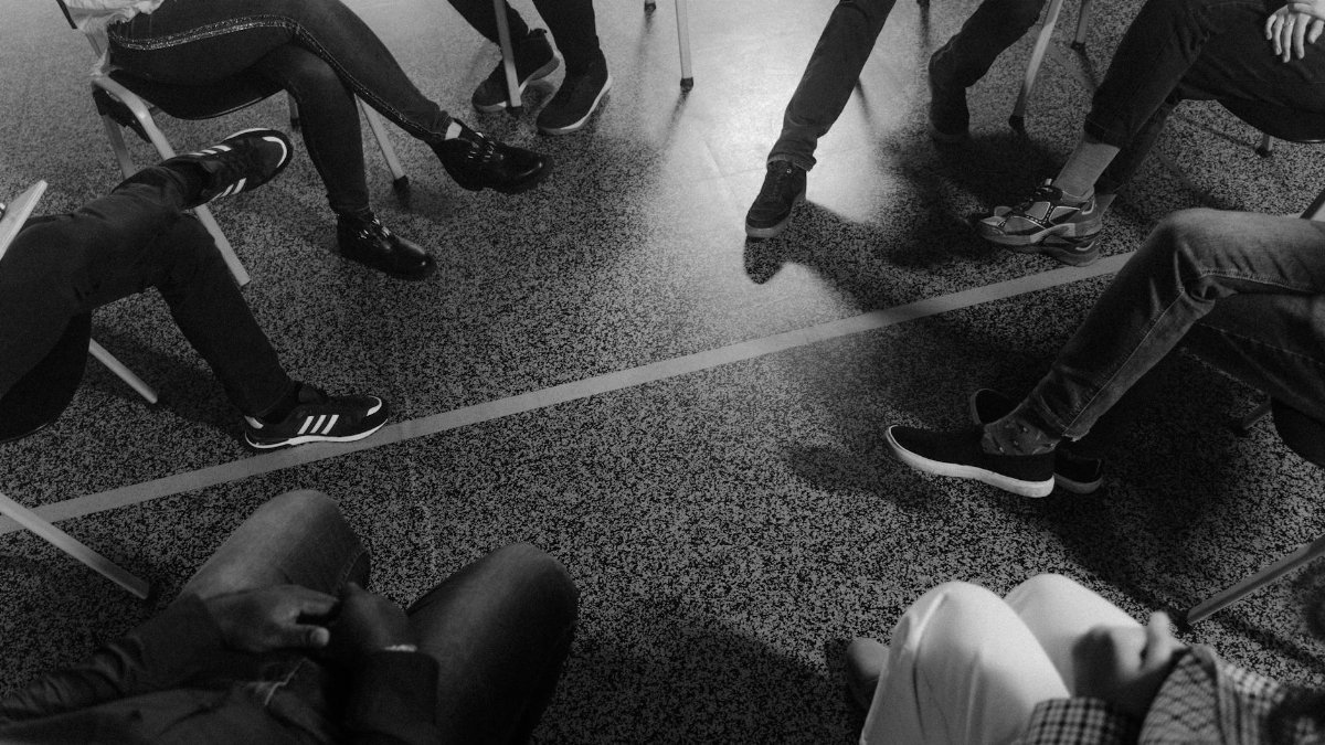 Black and white photo of a support group session indoors with diverse participants.