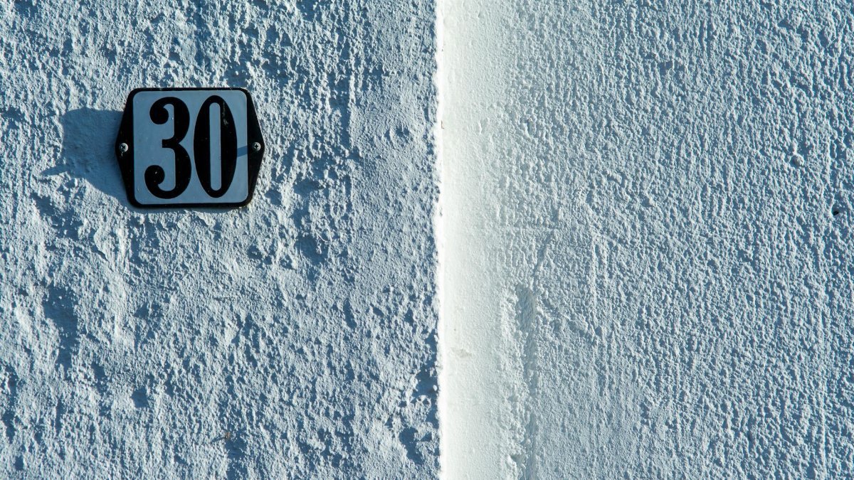 Close-up of a textured white wall featuring a classic house number 30 sign.