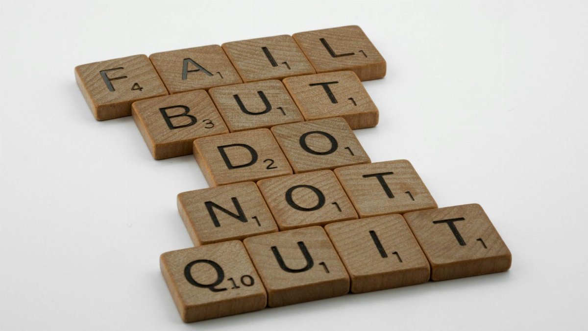 Close-up of Scrabble tiles forming the motivational phrase 'Fail but do not quit' on a white surface.