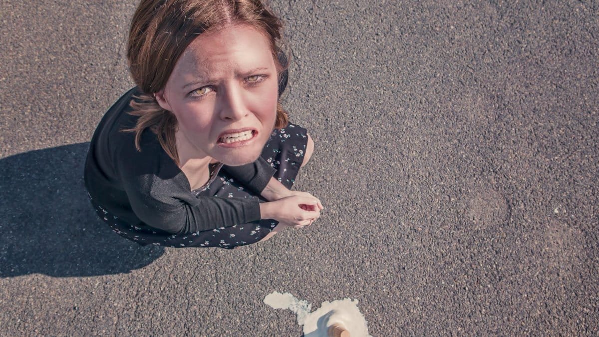 Aerial view of a frustrated woman on pavement next to spilled ice cream.