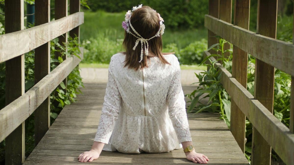 Back view of young woman with floral headband sitting outdoors on a wooden bridge.