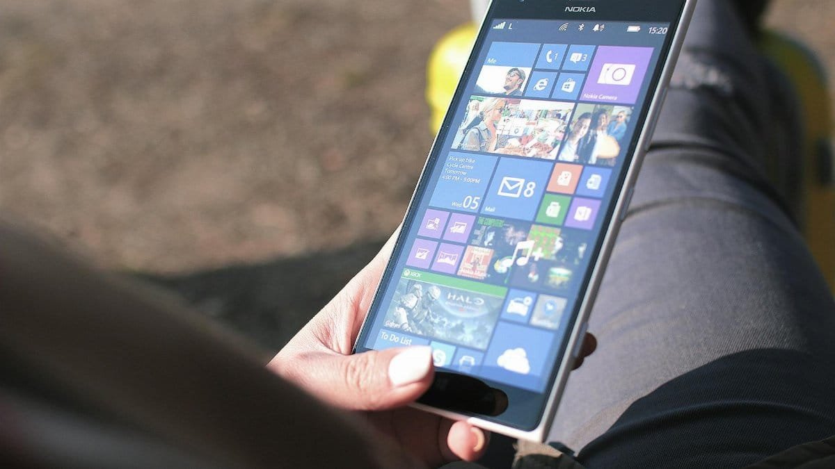 Close-up of a woman holding a Nokia smartphone running Windows operating system outdoors, showing touchscreen interface.