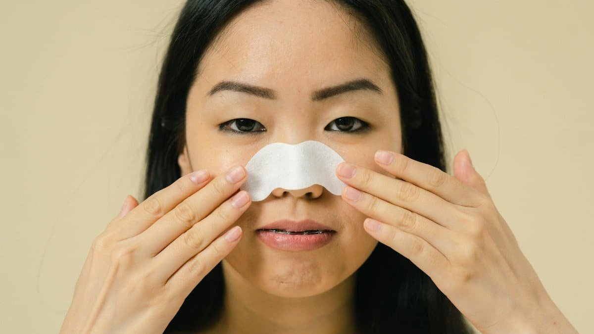 Close-up portrait of a woman using a nose strip for skin care treatment in a studio setting.