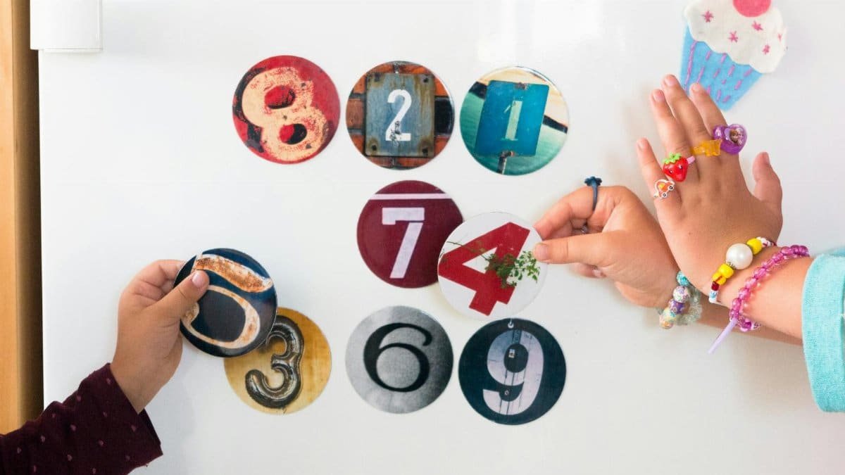 Two children playing with colorful number magnets on a fridge, engaging in a fun learning activity.