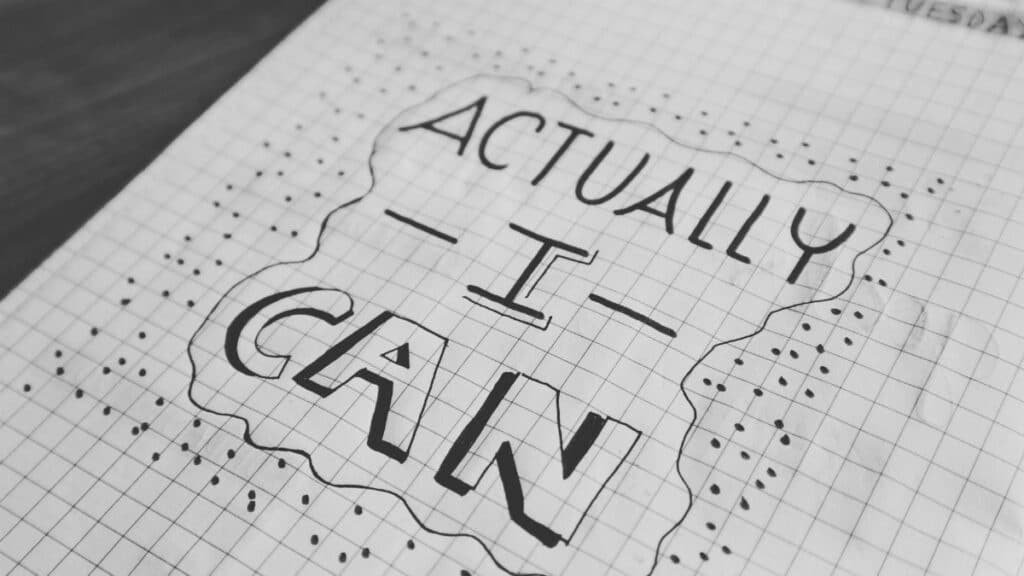 Motivational text 'Actually I Can' on a grid paper background. Black and white close-up.