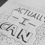 Motivational text 'Actually I Can' on a grid paper background. Black and white close-up.
