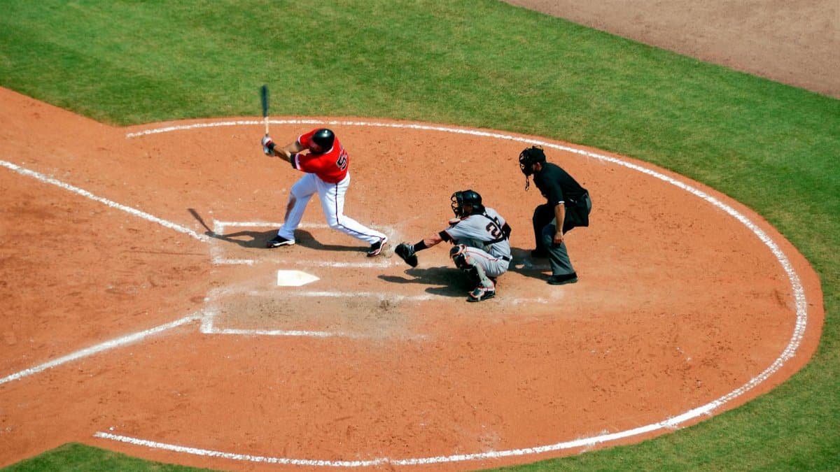 Action shot of a baseball game with batter swinging, catcher, and umpire observing play.