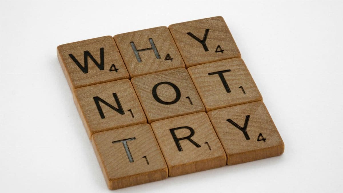 Wooden Scrabble tiles on a white background spelling the phrase 'Why Not Try'.