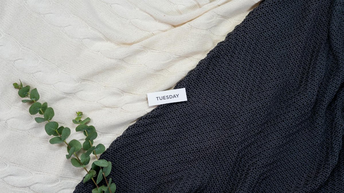 Warm woolen blankets with eucalyptus leaves and a Tuesday note create a cozy flatlay.