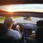 Driver using phone while driving at sunset with passenger in vehicle.