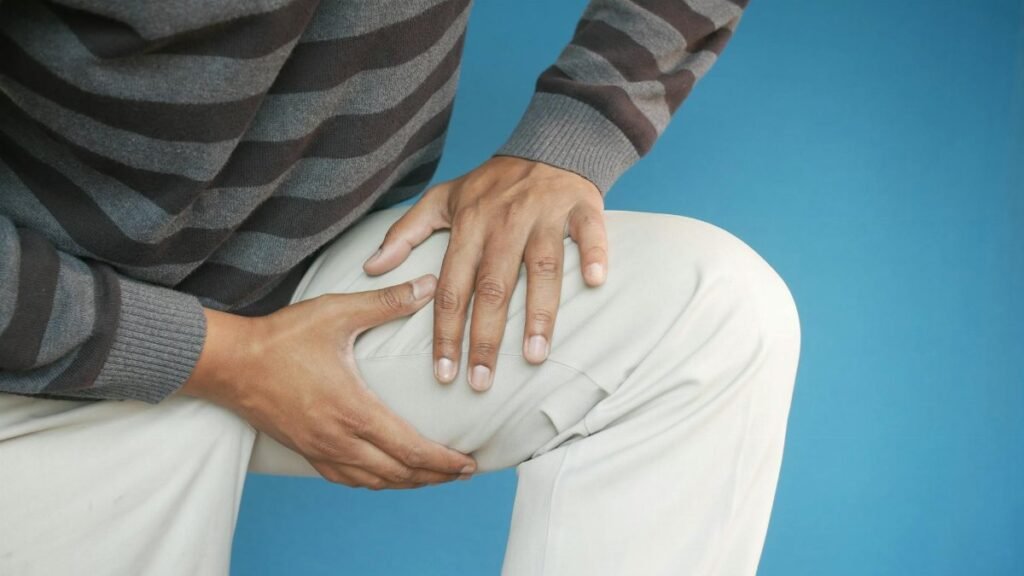 Close-up of a man's hands on his knee, showing pain or injury, on a blue background.